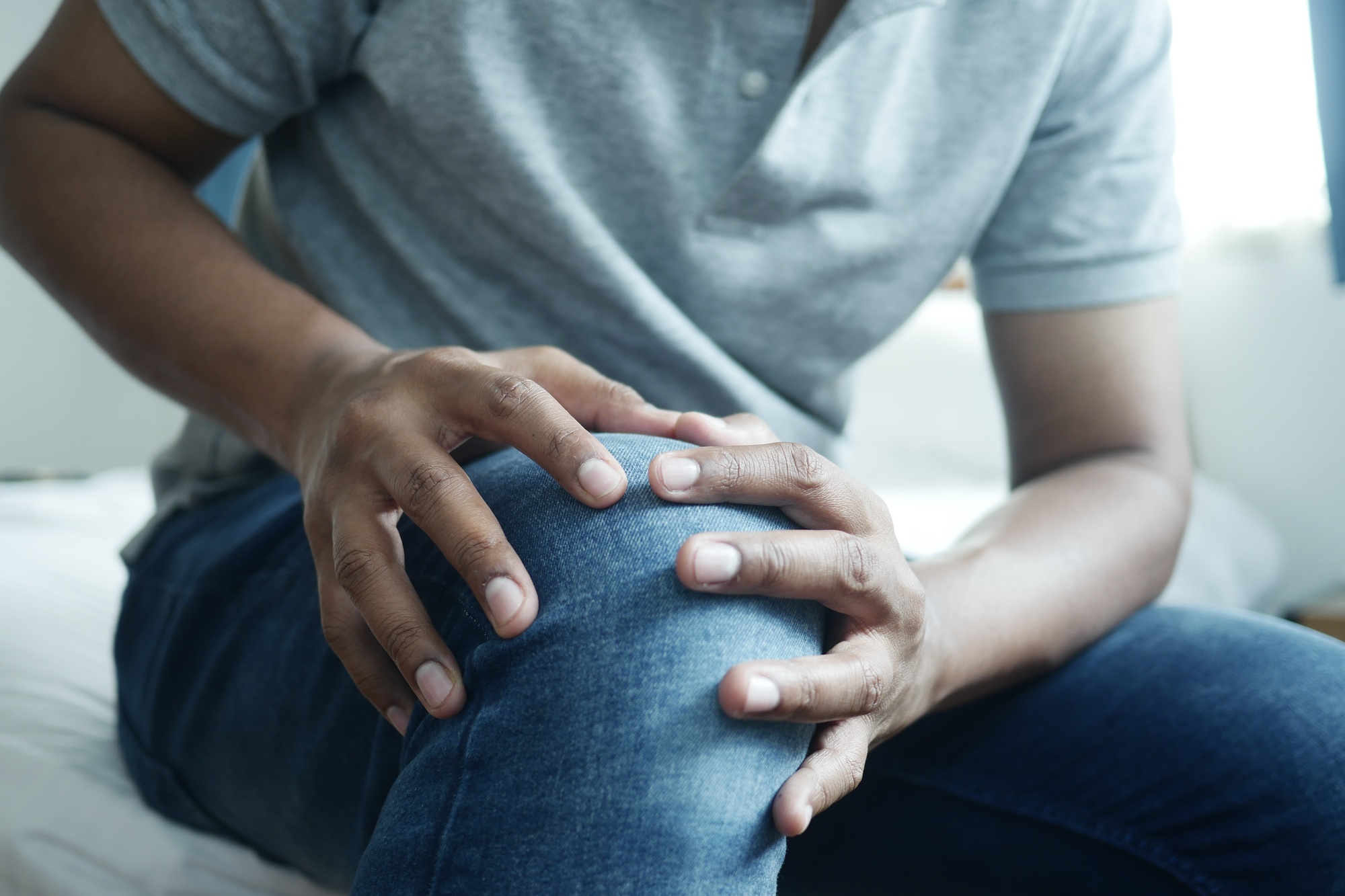 An elderly or middle-aged person experiencing knee pain, showing symptoms like swelling or stiffness around the knee, set in a Malaysian urban environment such as Sungai Buloh.